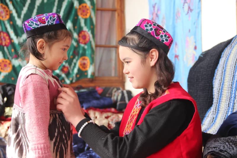 Singlisining an’anaviy kiyimini to‘g‘rilayotgan yosh qiz
