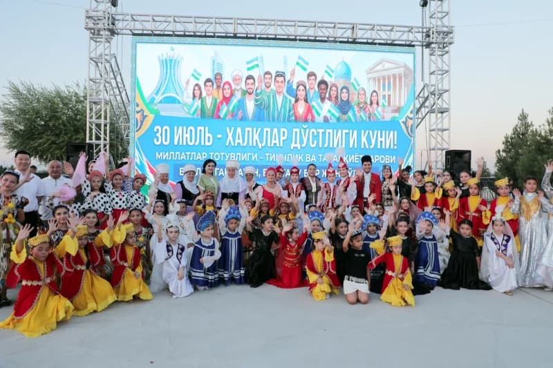 Люди в различных костюмах позируют перед большим экраном на открытом воздухе