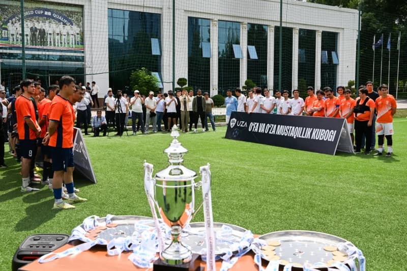 Groups of soccer players stand on a field with a trophy and banners