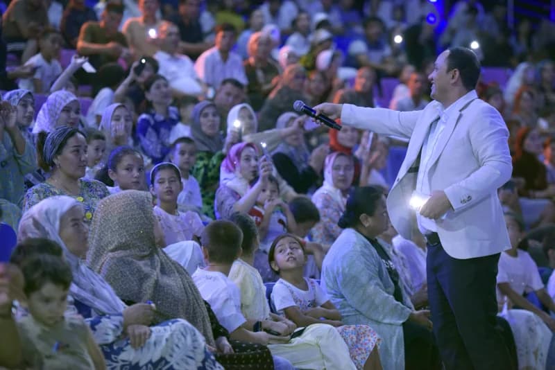 People gathered in a large seated audience watching a speaker hold a microphone