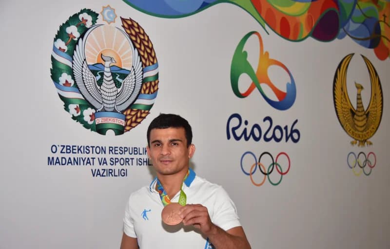 Rasmiy ramzlar oldida medal ushlab turgan sportchi
