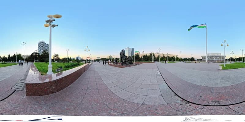 Public square with a monument, flag, and surrounding urban buildings
