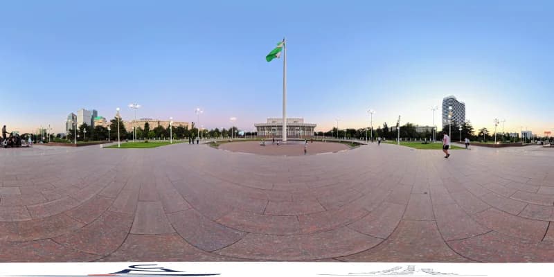 Panoramic view of a large public square with a flag pole and buildings