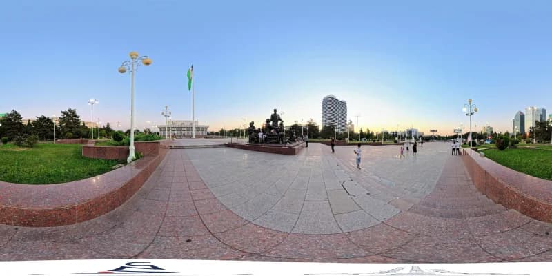 People walk on a public plaza with a monument and flag