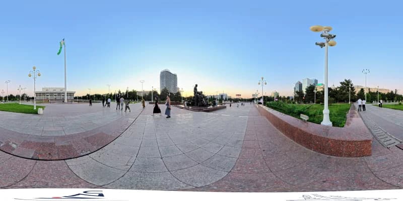People walking on a paved city square with a monument and flag