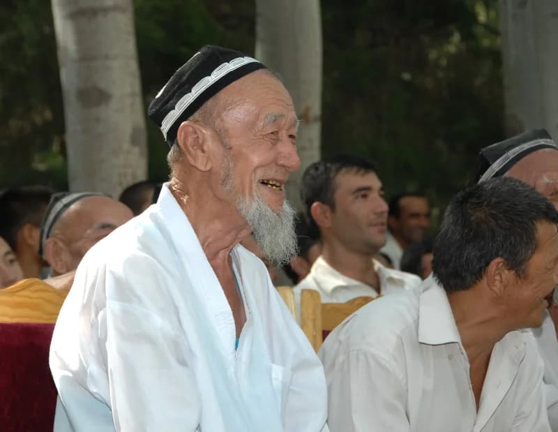 Smiling senior man wearing a traditional cap and white robe among people