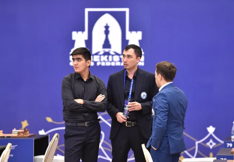 Three men standing together in front of a blue backdrop with chess motifs
