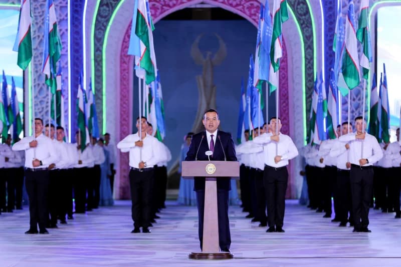 Person speaking at a podium before a line of flag-bearers