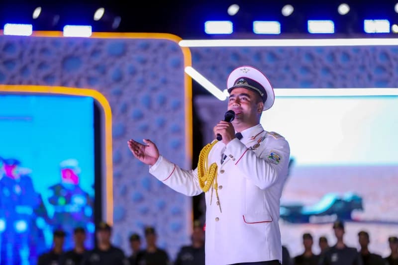 Person in military-style uniform speaking into a microphone on stage
