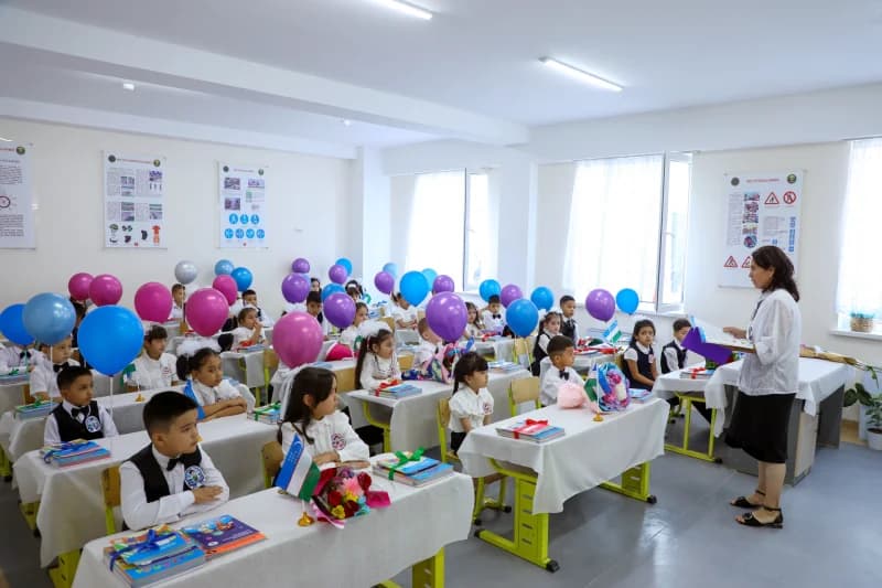 Дети сидят за партами в классе с воздушными шарами.