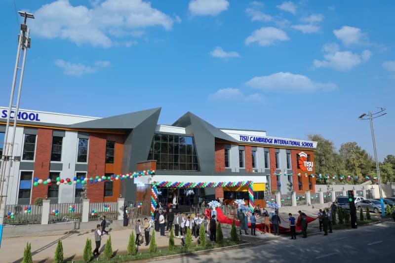 People gathered in front of a modern school building decorated with colorful balloons