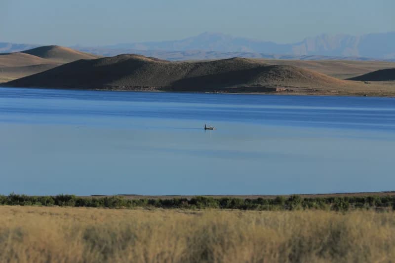 Boat on a wide lake surrounded by hills and distant mountains