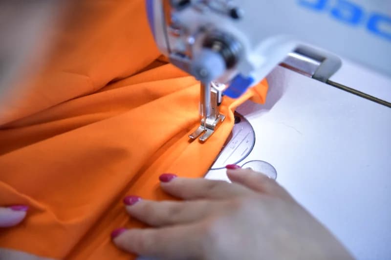 Person sewing orange fabric on a sewing machine