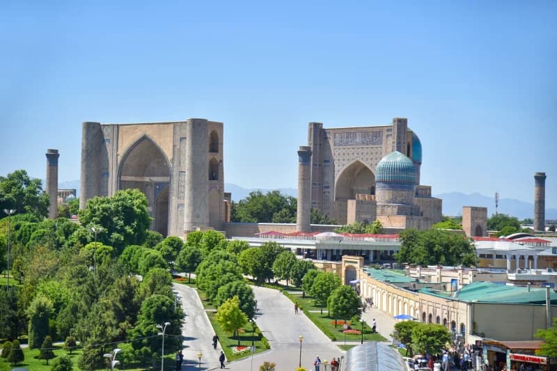 Historic architectural complex with large arched entryways and blue domes under a clear blue sky