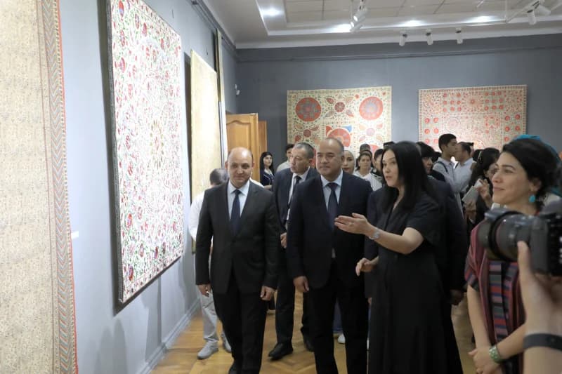 People touring an exhibition hall displaying large embroidered textiles