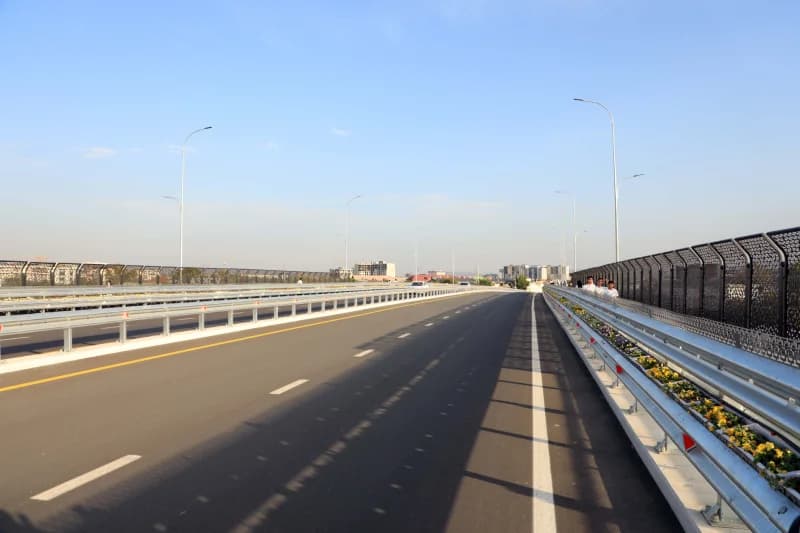 View of a wide asphalt road on a bridge with safety barriers and pedestrian walkways