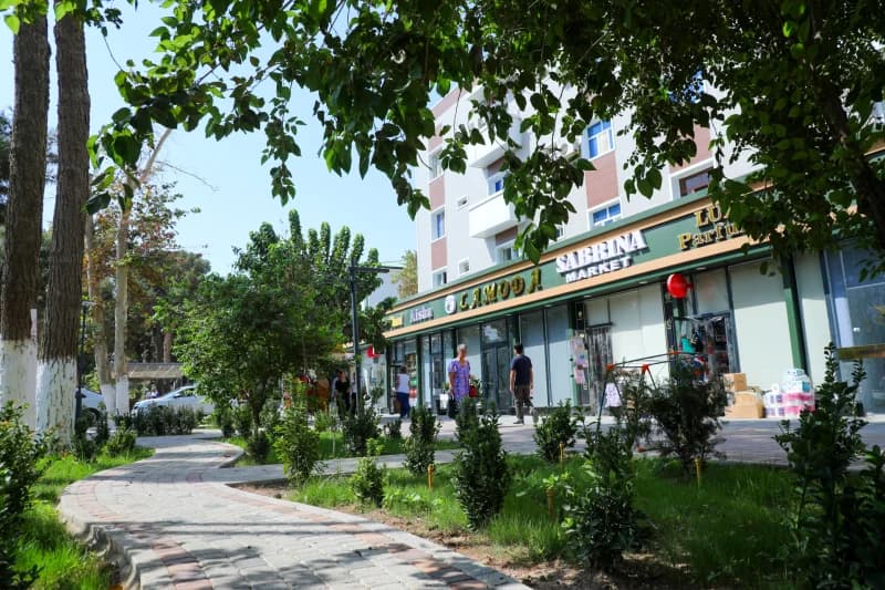 People walking along a paved walkway near commercial storefronts