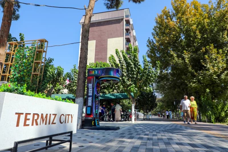 People walking along a paved walkway lined with trees and a building in the background
