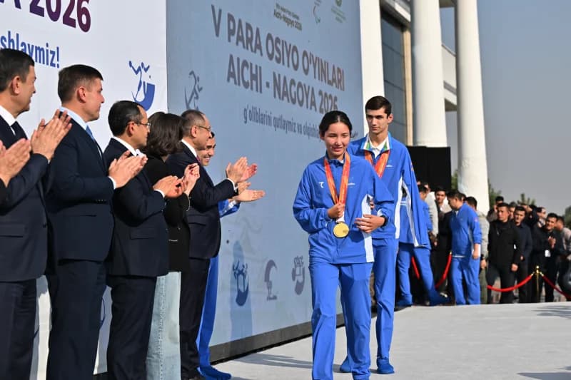 Athletes in sportswear walking past a clapping crowd in front of a branded backdrop