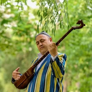 Ochiq havoda anʼanaviy torli cholgʻu chalayotgan odam