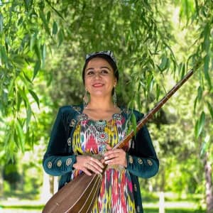 Ochiq havoda musiqa asbobini ushlab turgan anʼanaviy kiyimdagi ayol