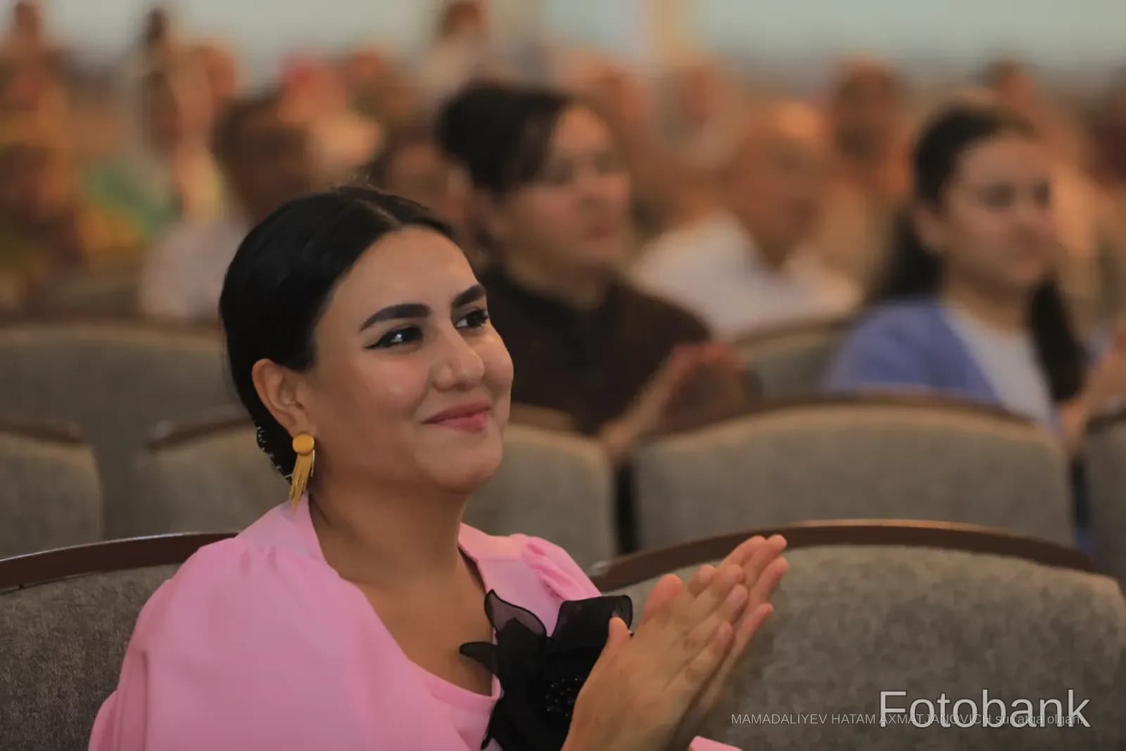 Auditoriyada tabassum qilayotgan va qarsak chalayotgan ayol