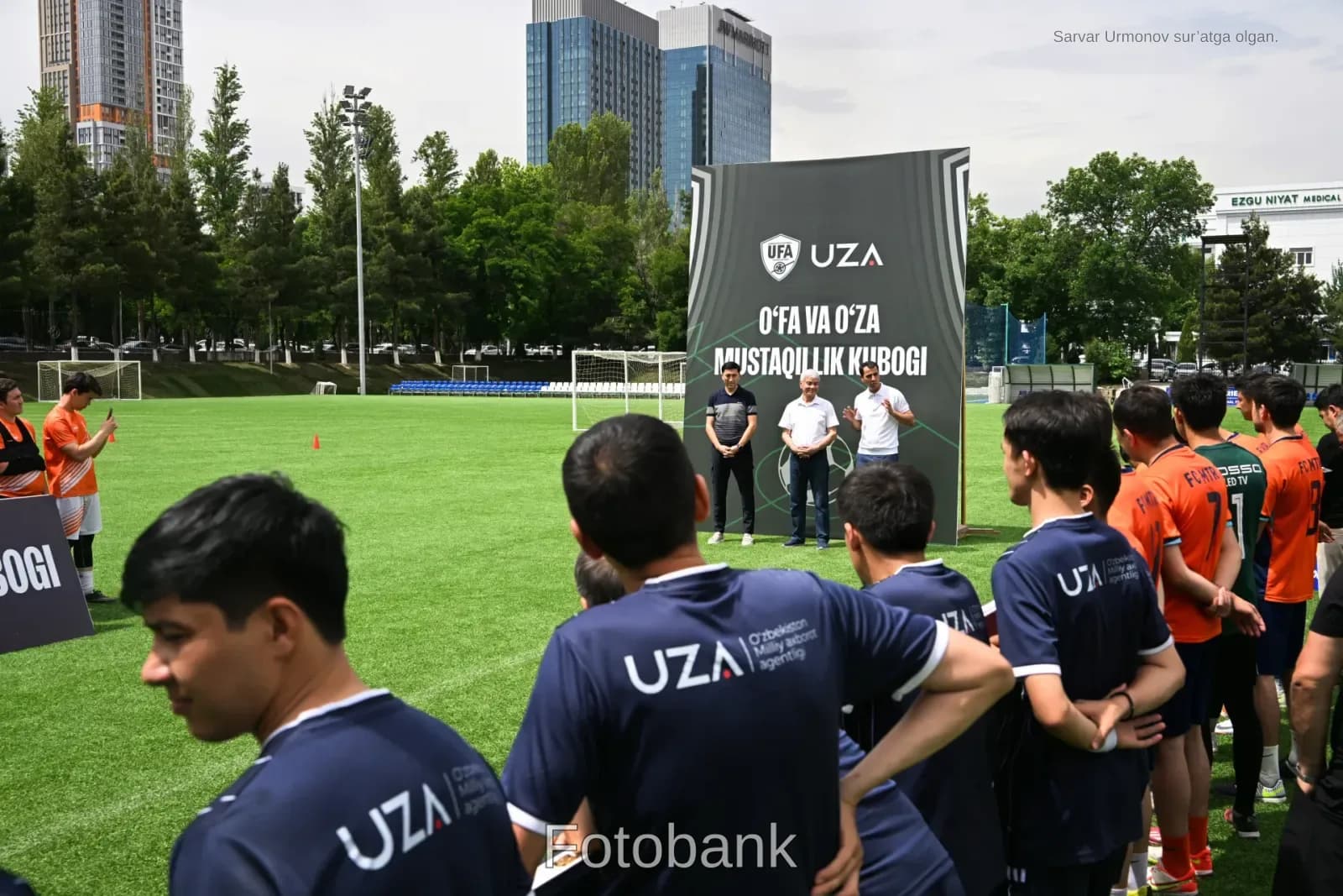 Futbol maydonida banner bilan toʻplangan odamlar.