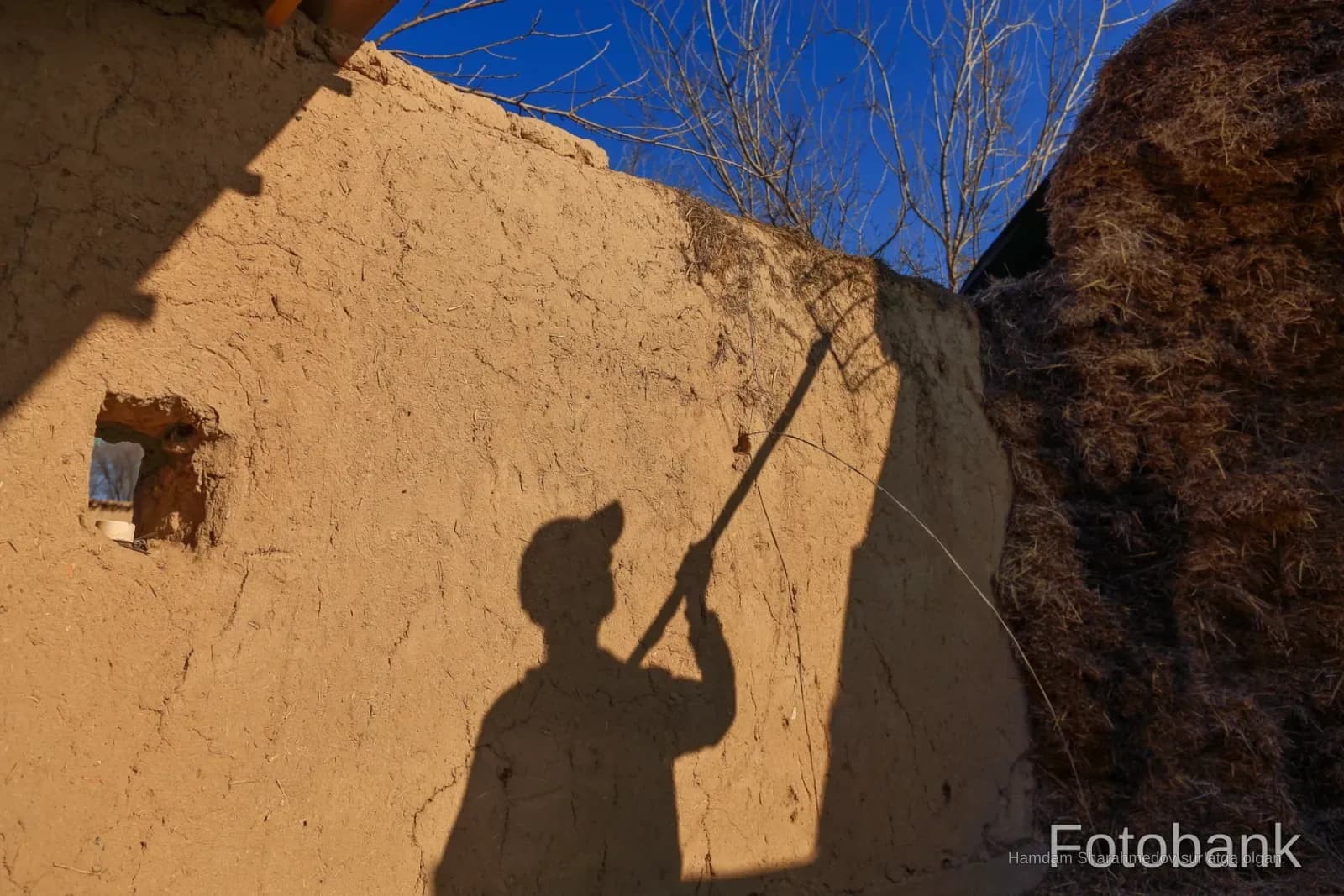 Shadow of a person holding a tool against a mud wall