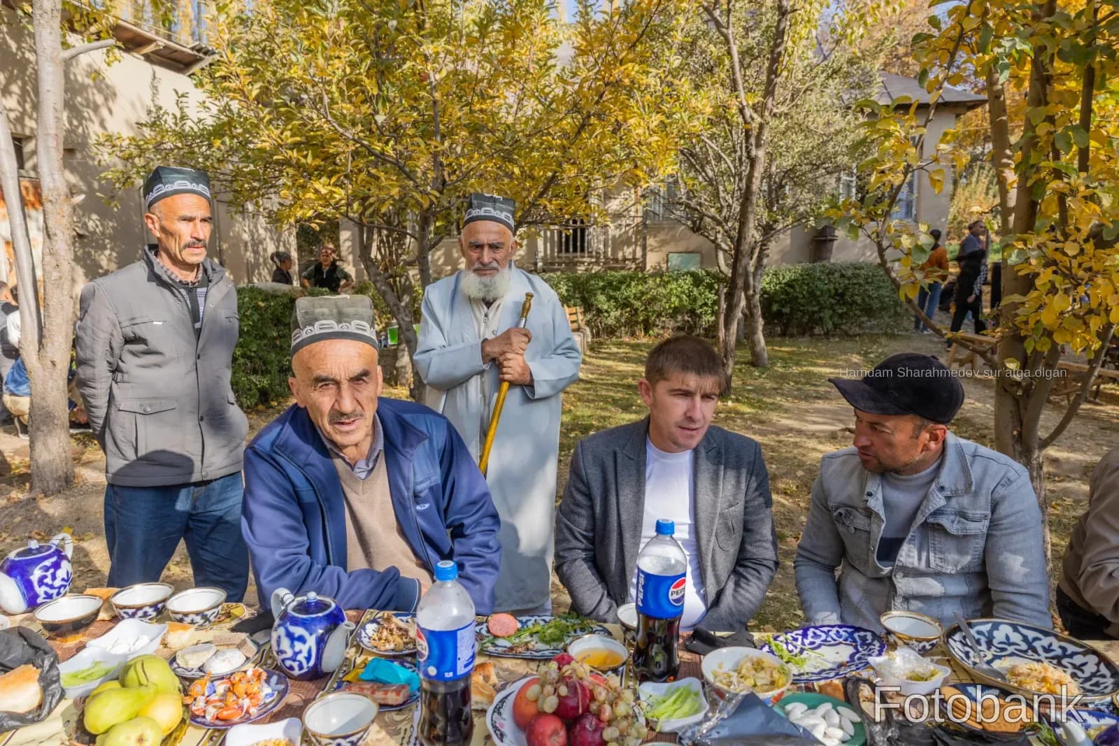Group of men gathered outdoors around a table laden with food and drinks