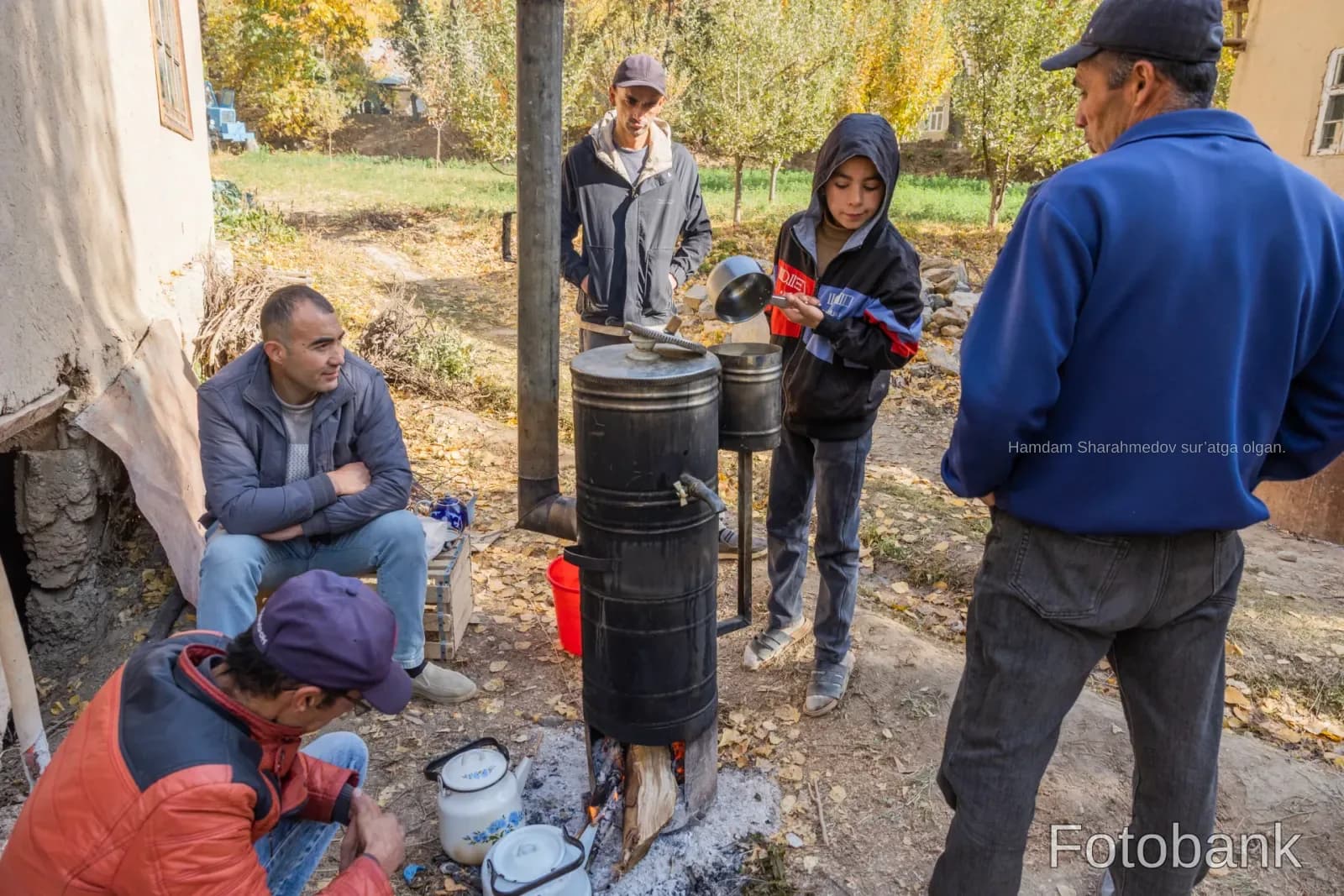People gathered outdoors around a wood burning stove in a rural setting