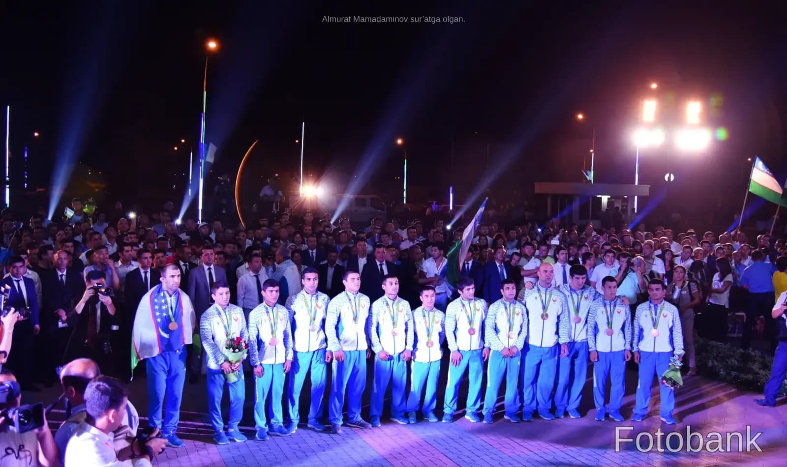 Group of athletes wearing medals standing outdoors at night