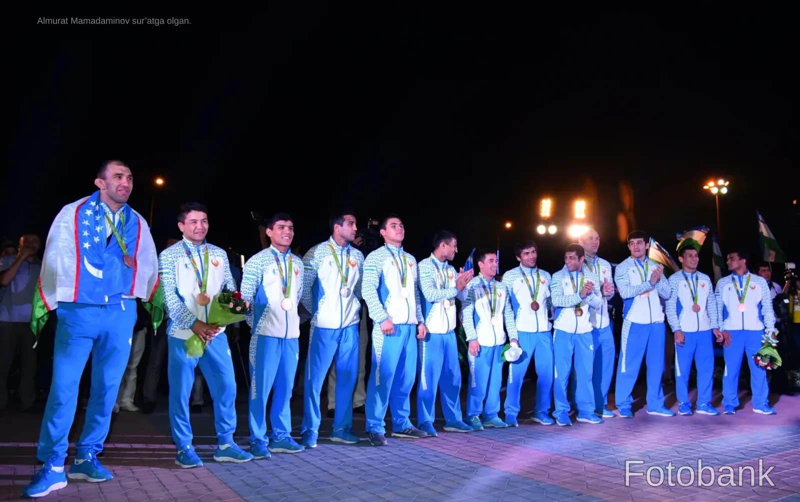 Athletes standing in matching sportswear with medals at night