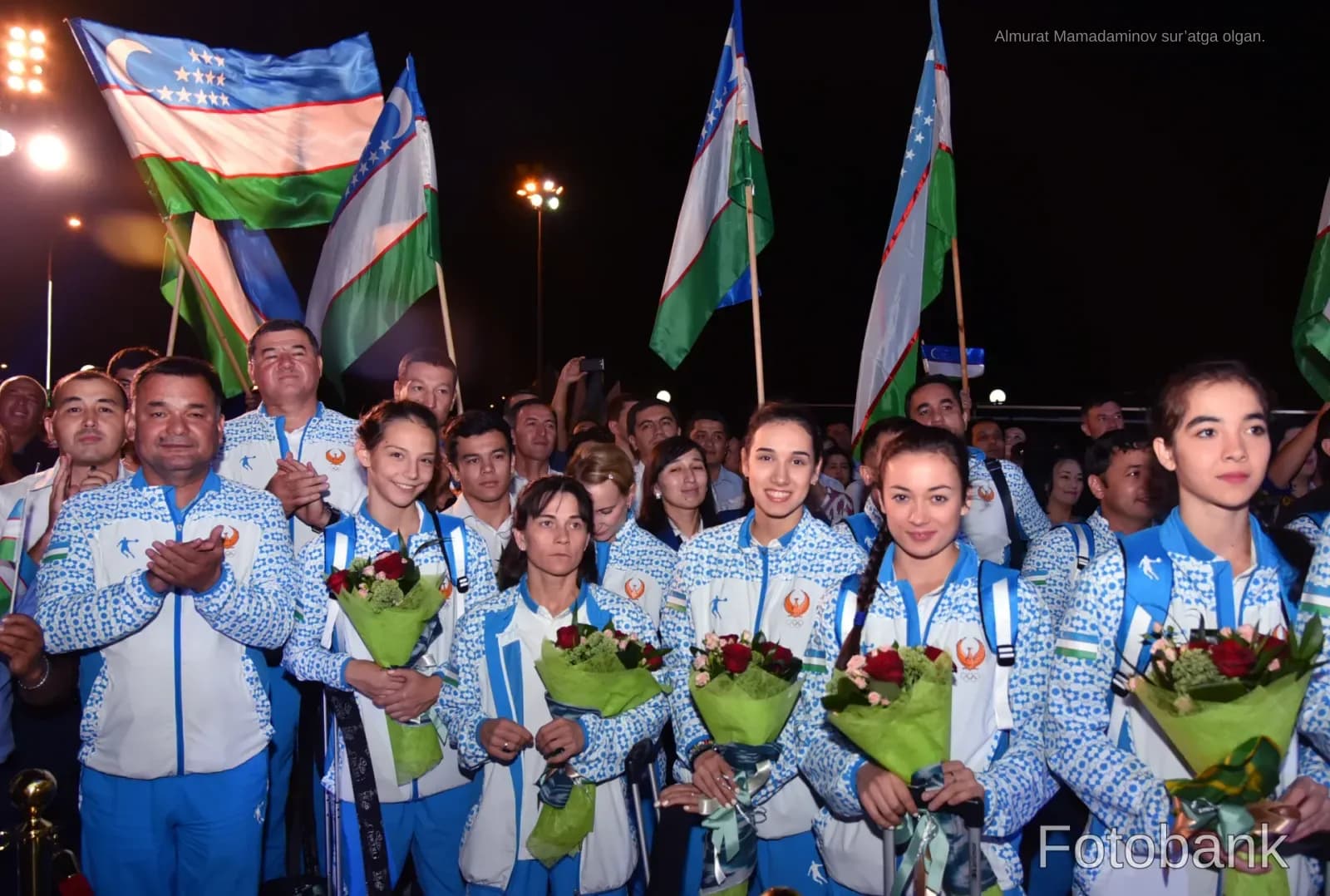 Athletes holding flags and bouquets outdoors at night