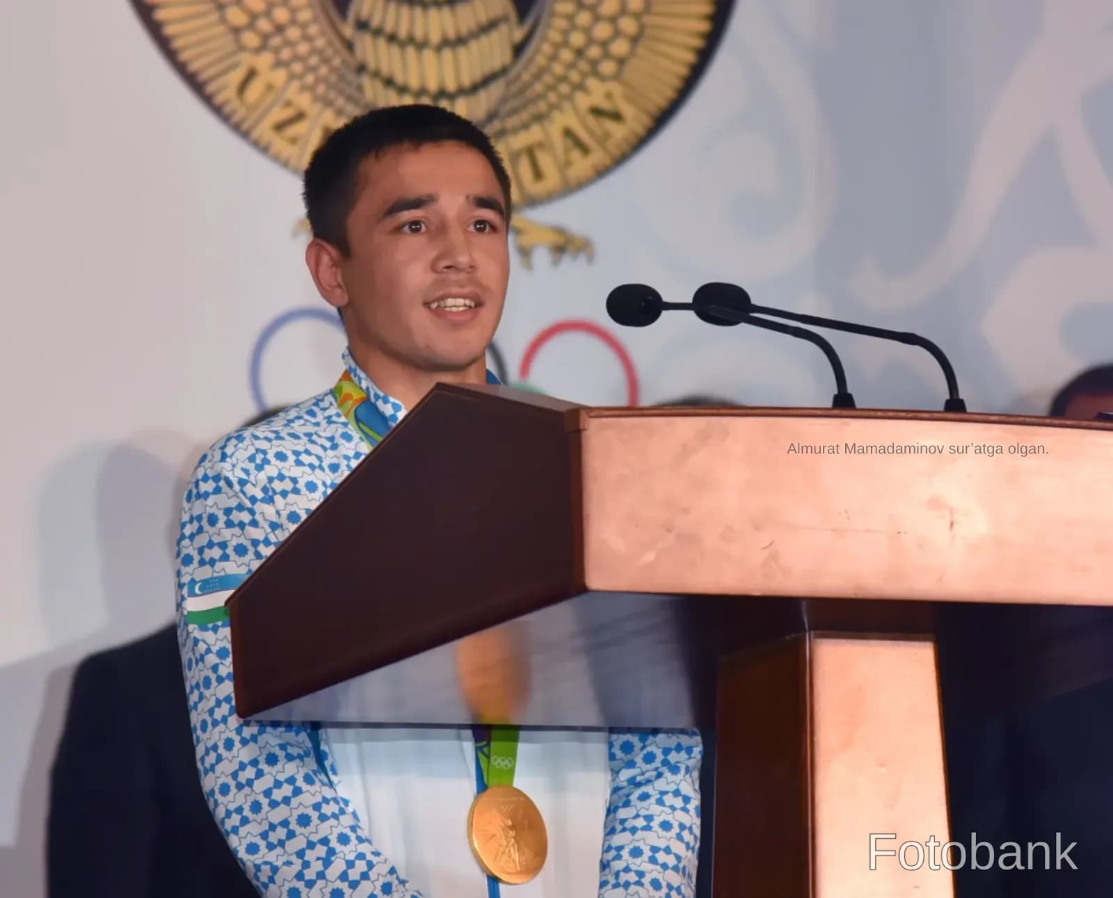 Young man speaking at a podium with a medal around his neck