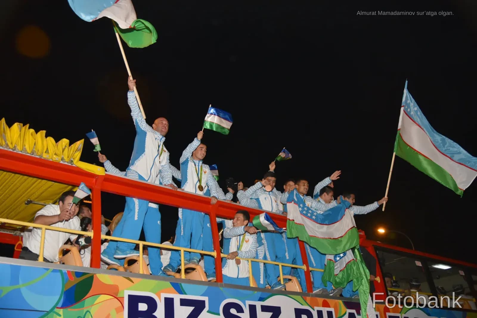 People waving flags and celebrating on top of a vehicle at night