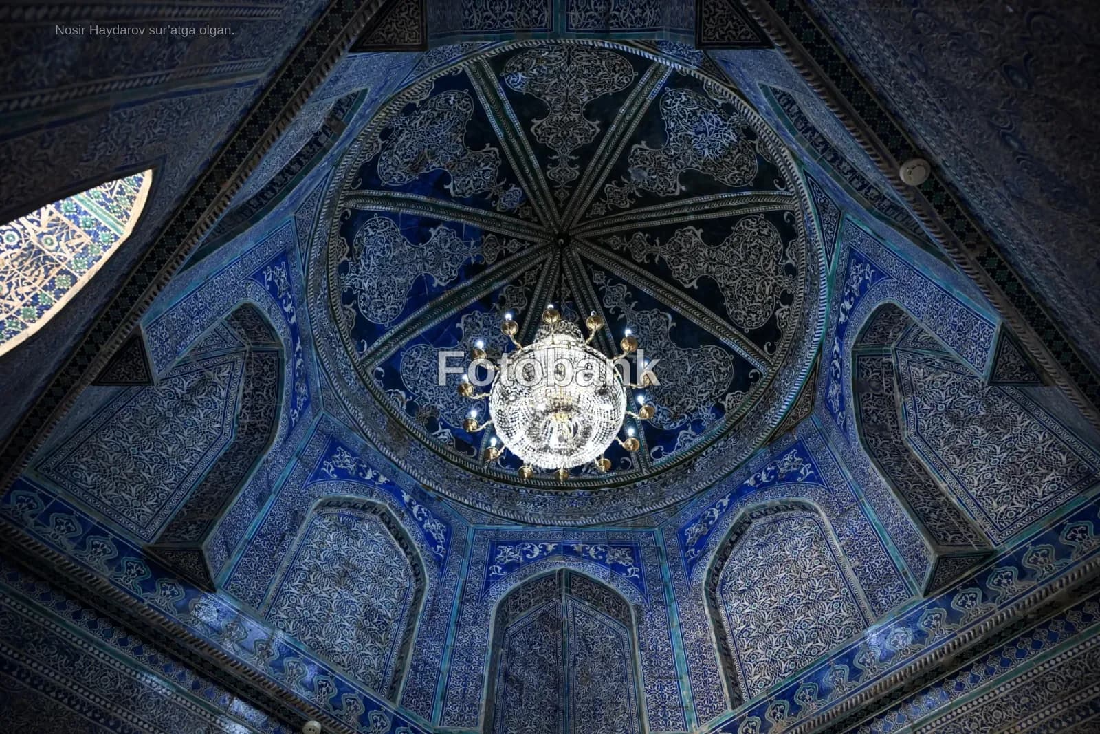 Intricate blue tilework and chandelier inside a historic domed structure