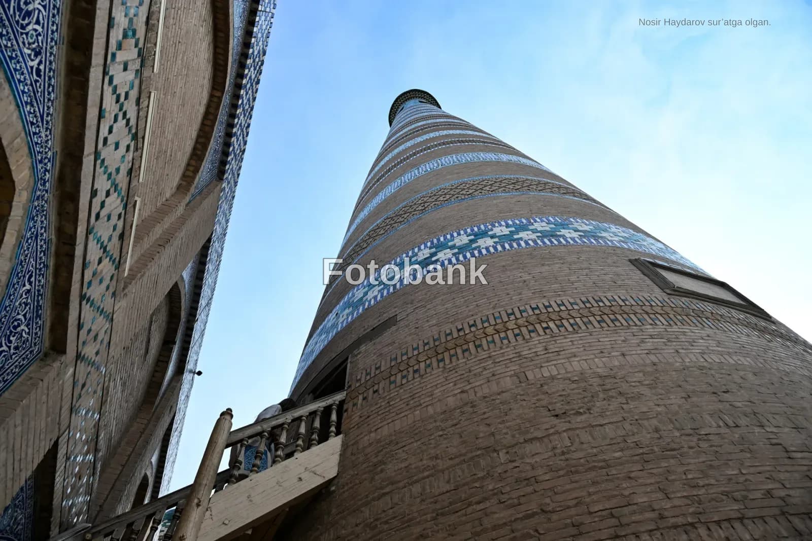 Low angle view of tall brick minaret with geometric tile bands and adjacent historic building