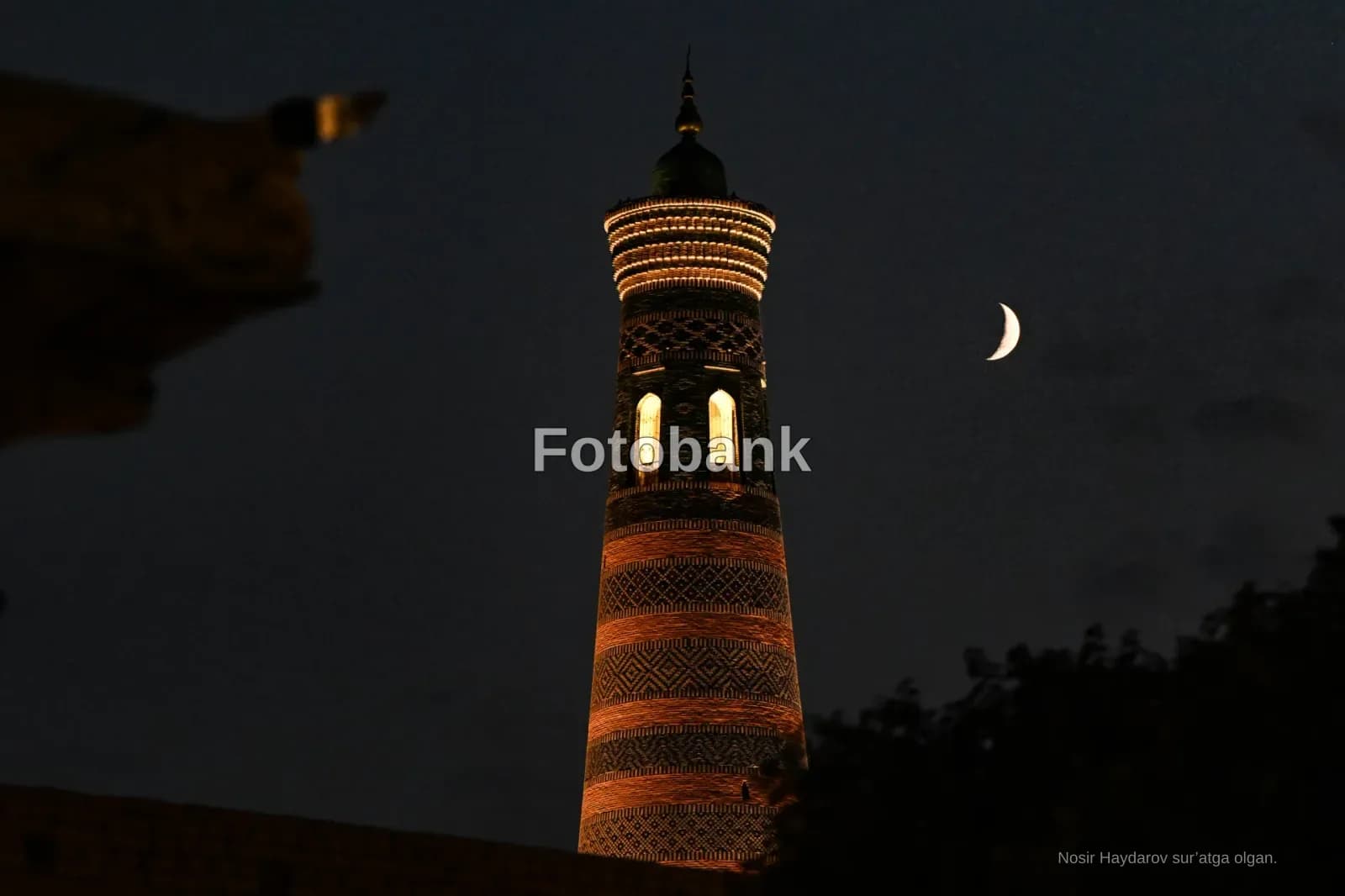 Illuminated minaret at night with a crescent moon