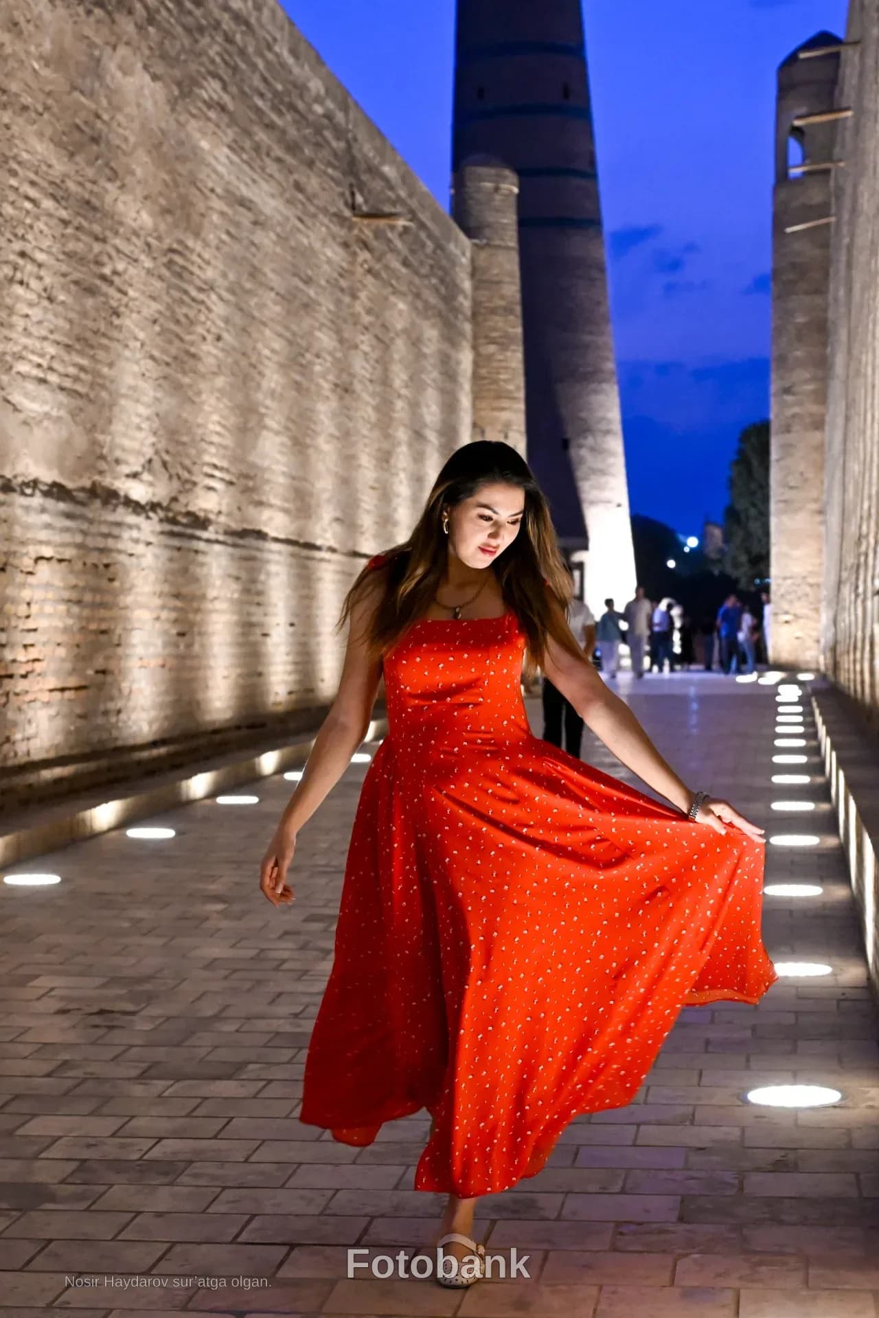 Woman in red dress walking along ancient illuminated street at dusk