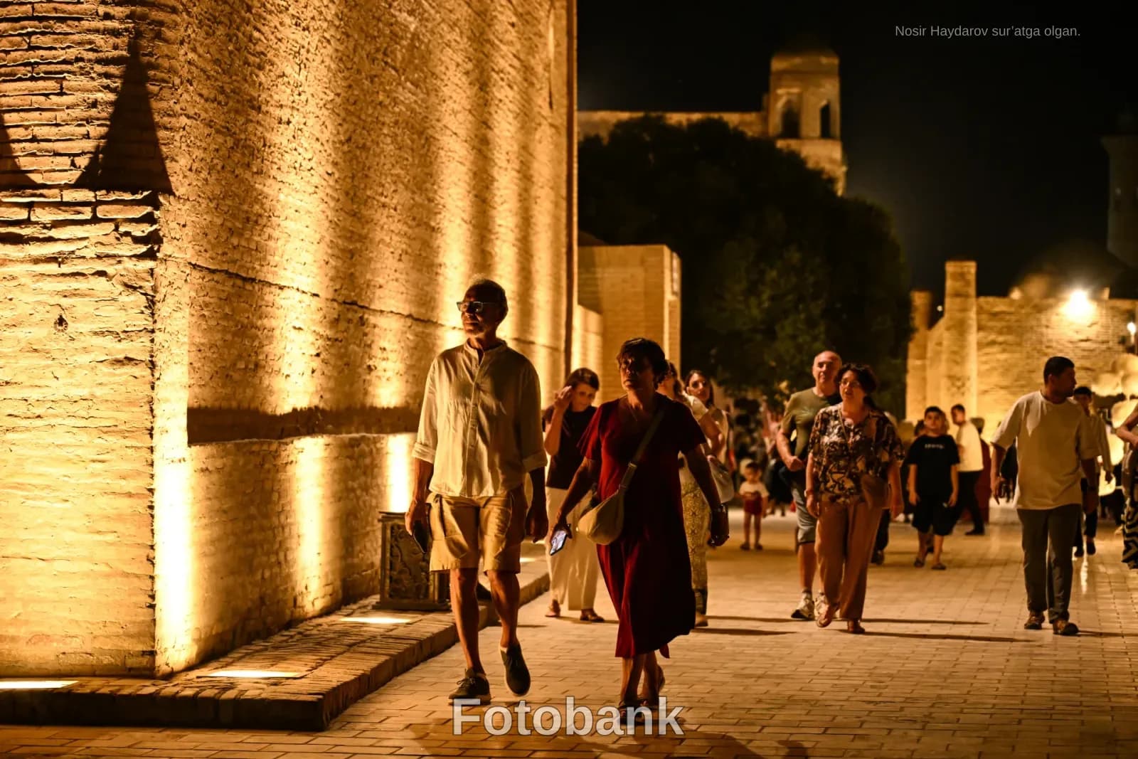 People walking outdoors at night along an illuminated historic wall