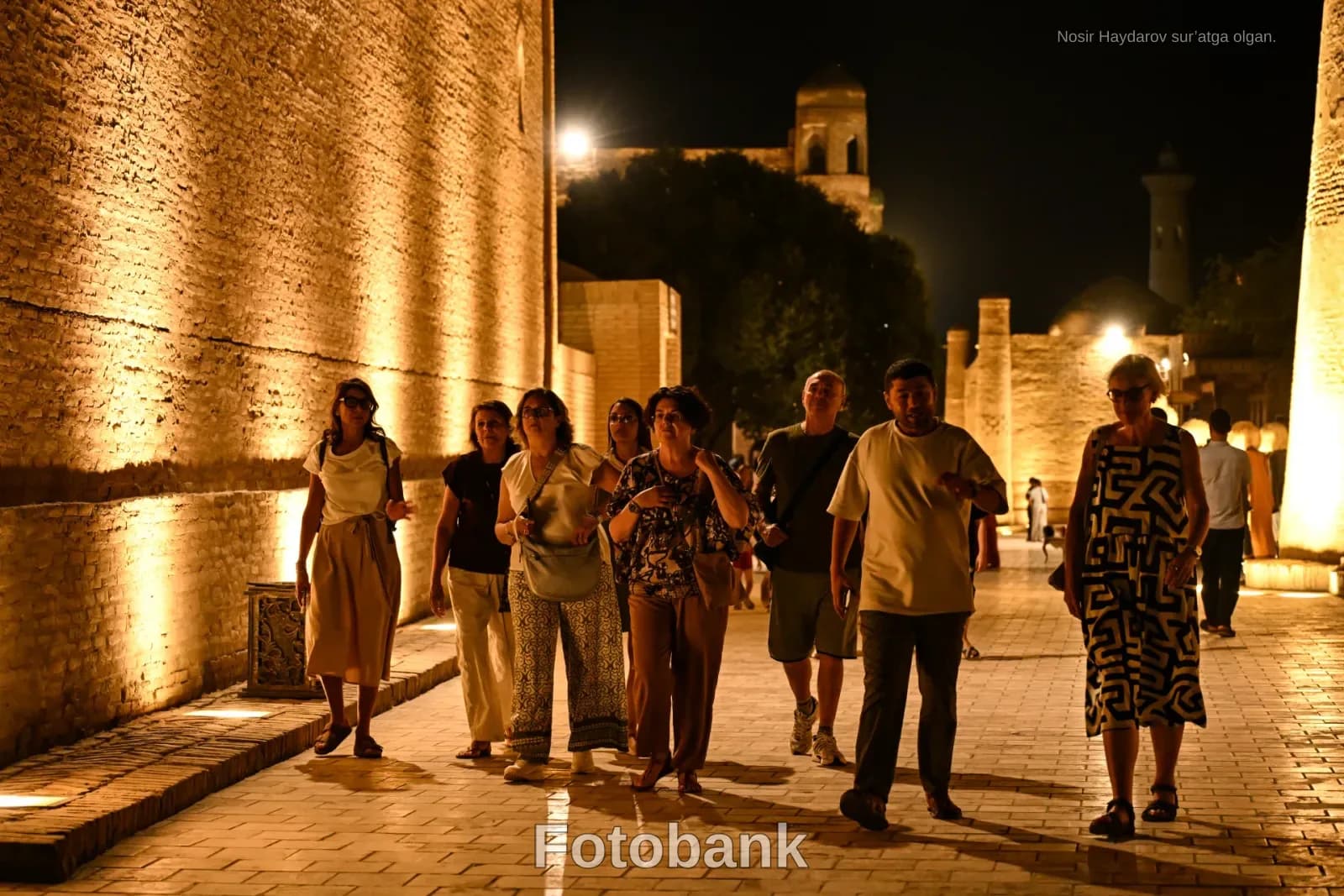 People walking on an illuminated brick walkway at night
