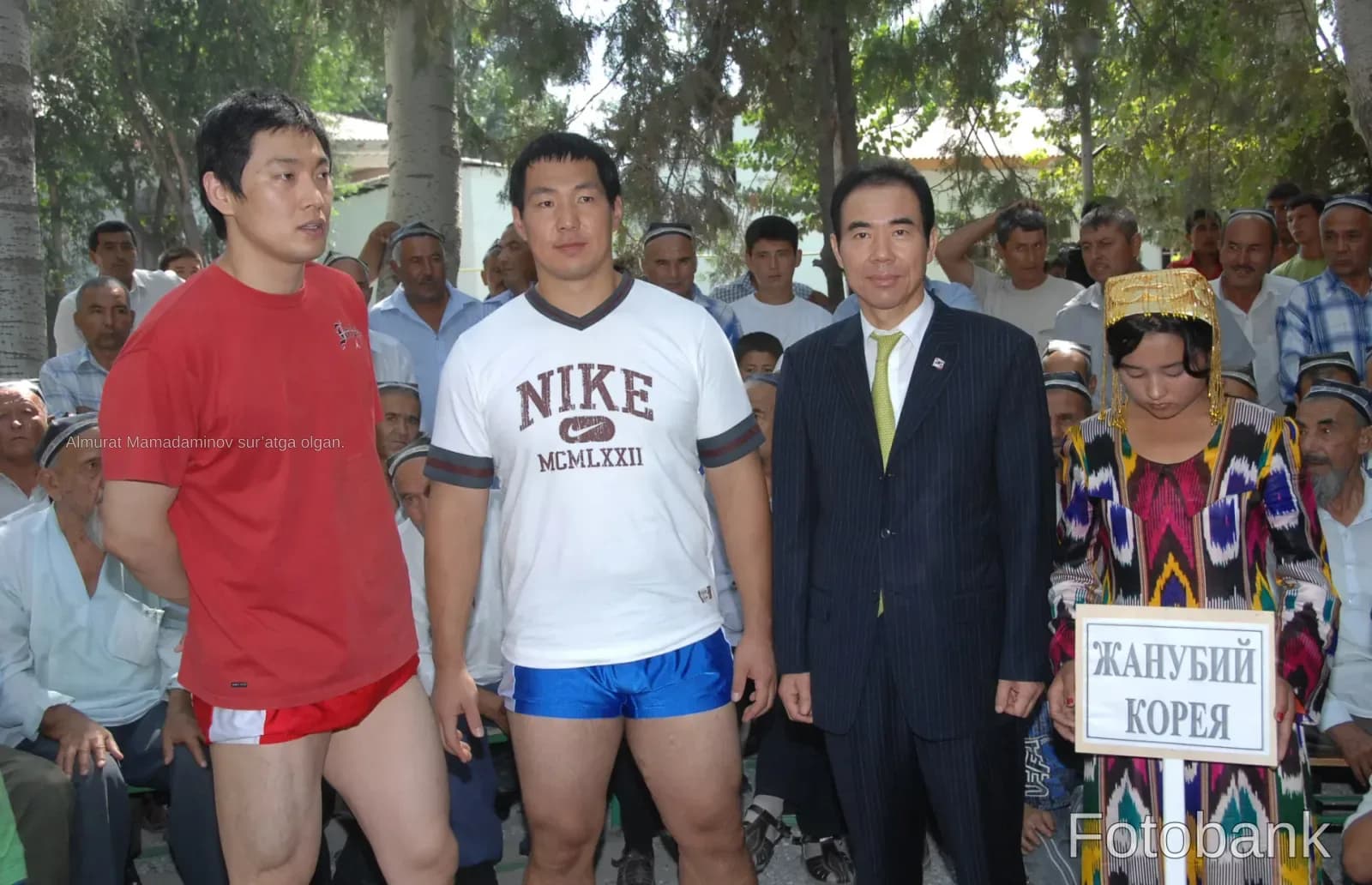 Group portrait of people outdoors including men in athletic wear and a person holding a sign