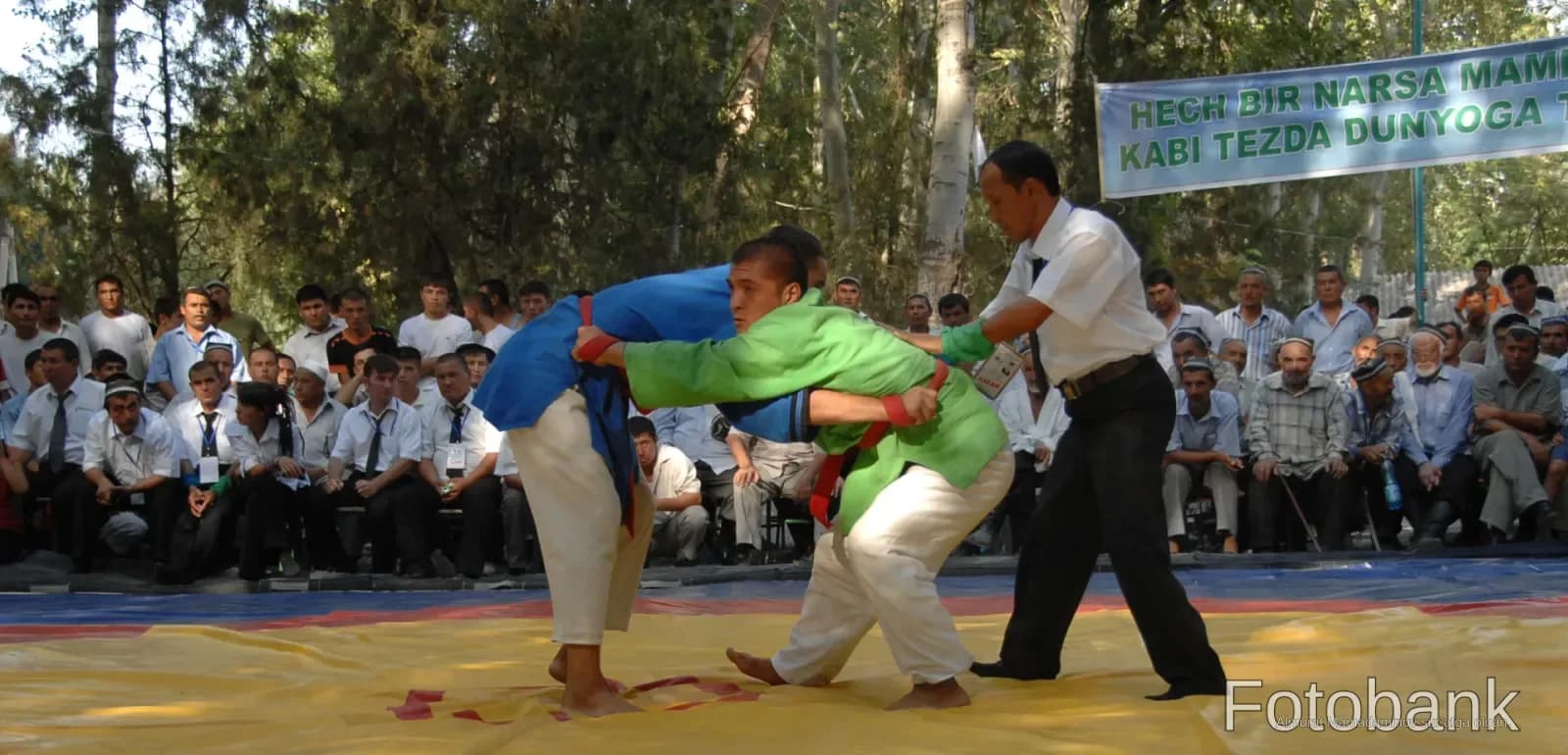 Wrestlers competing on an outdoor mat watched by spectators