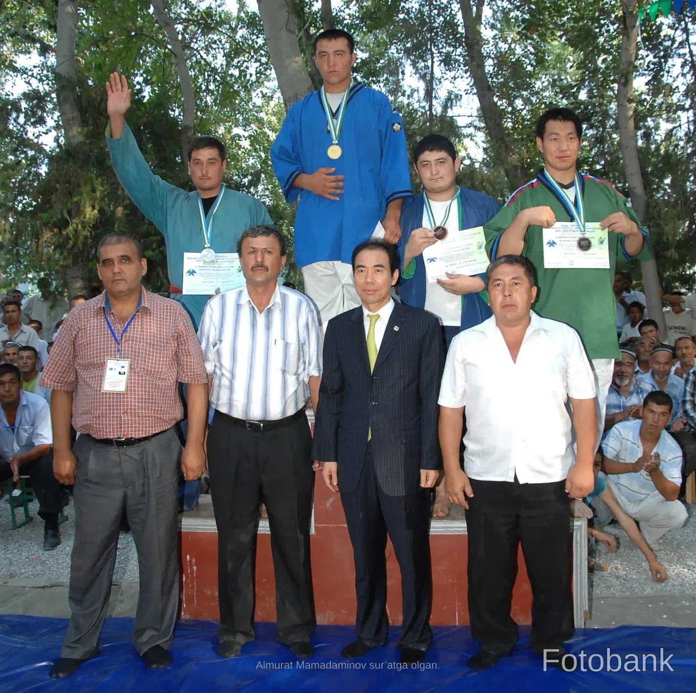 Athletes and officials pose on a stage outdoors