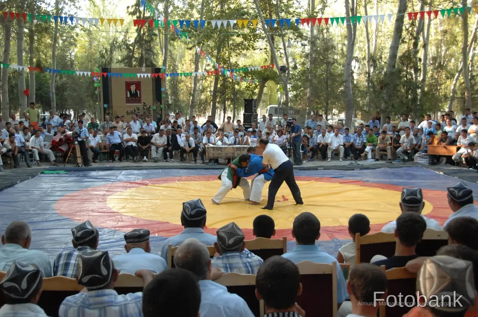 Wrestlers competing on an outdoor mat before a seated audience