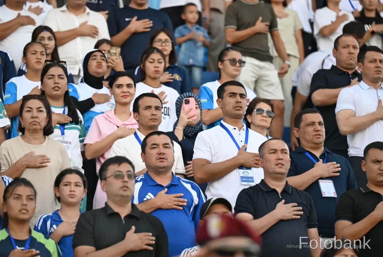 Crowd of people standing with hands on chests in stadium