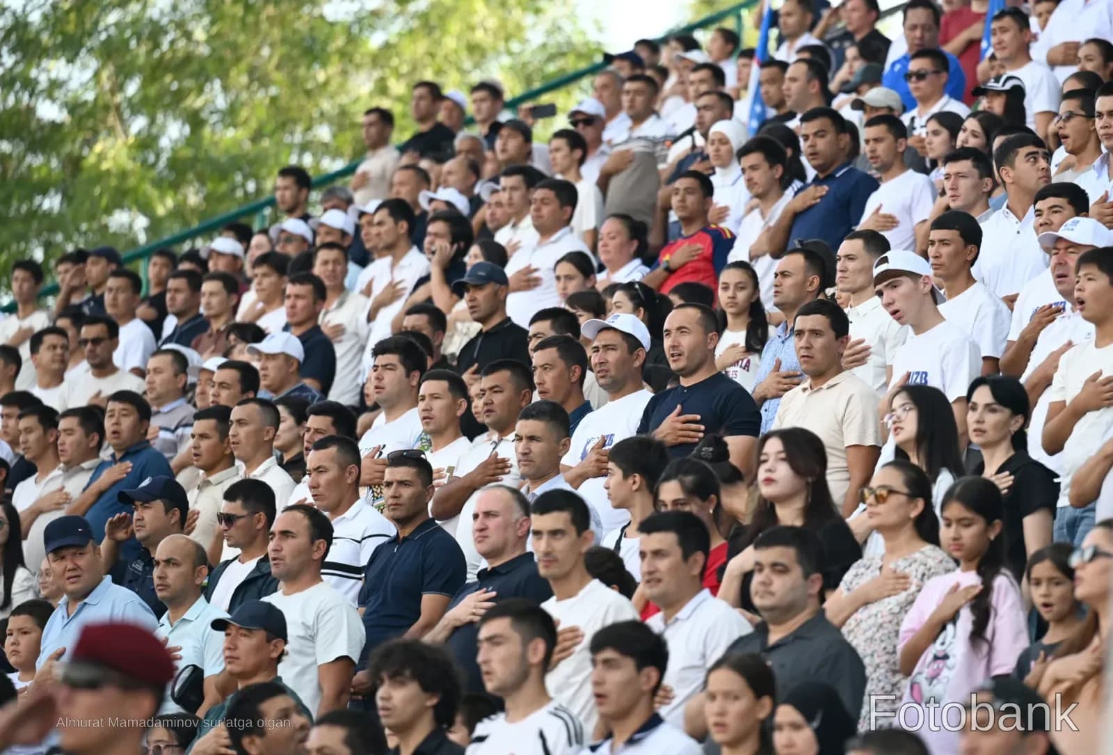 Crowd of people standing with hands on chests in stadium bleachers