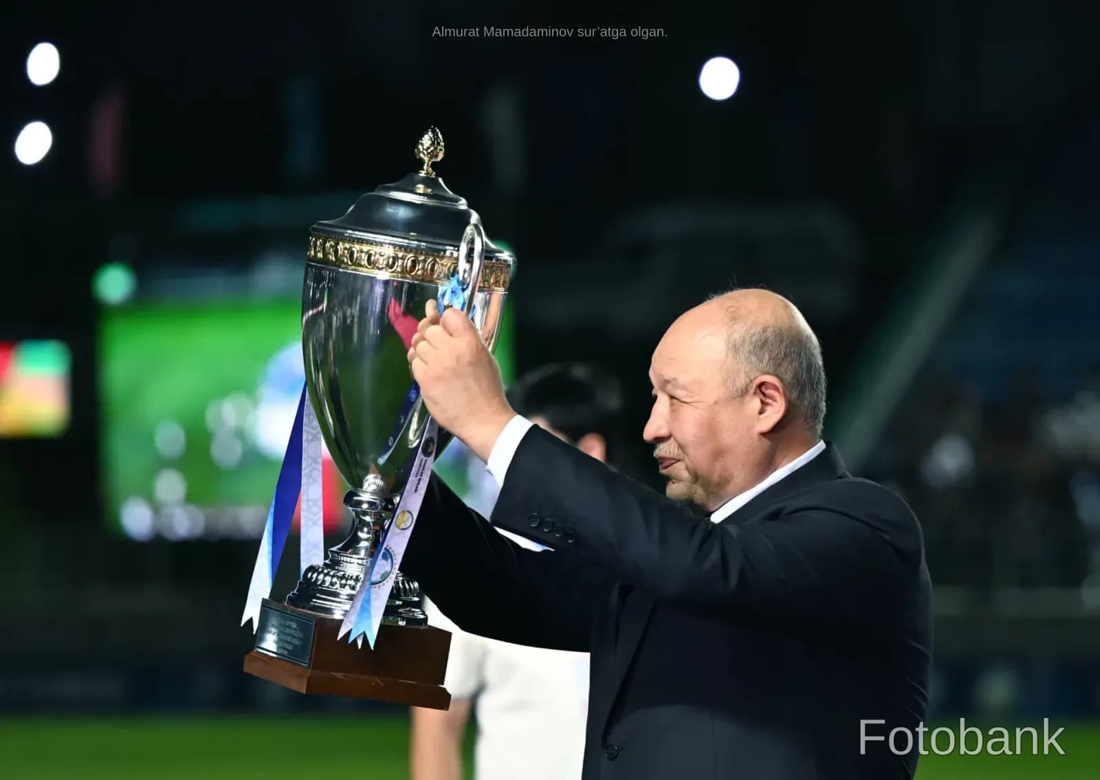 Мужчина держит большой кубок на стадионе