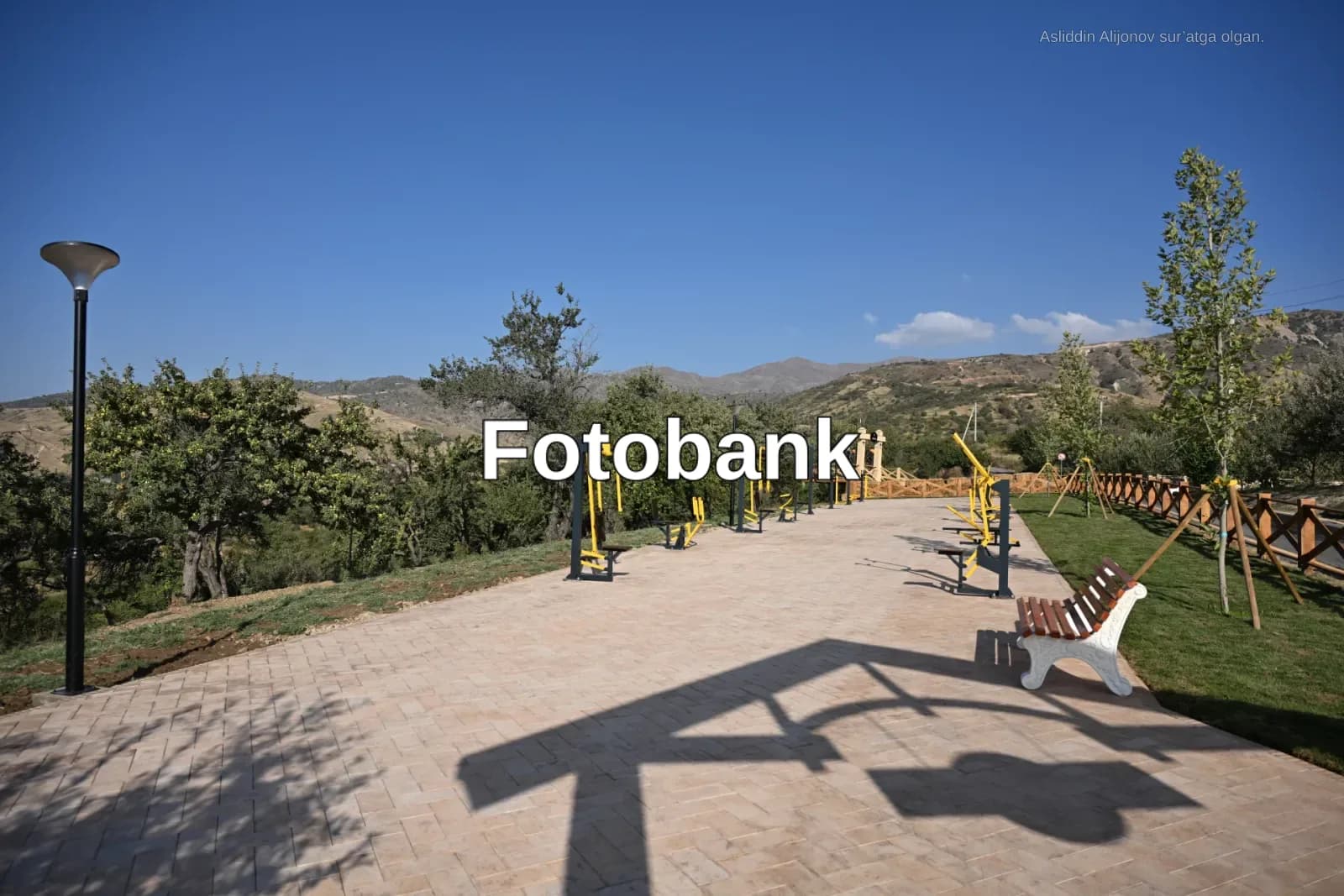 Togʻli landshaftda asfaltlangan yoʻl boʻylab oʻrnatilgan ochiq fitnes jihozlari