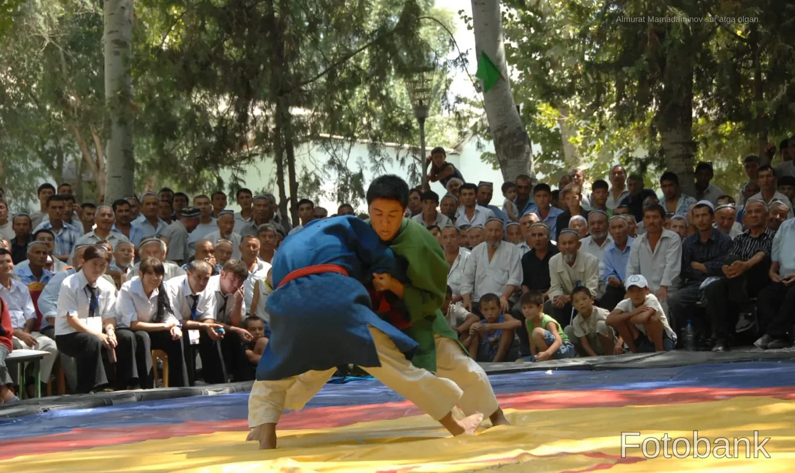 Competitors grapple on a mat during an outdoor wrestling match